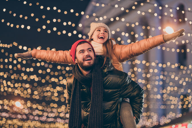 girlfriend backriding on boyfriends back with christmaslights in the background